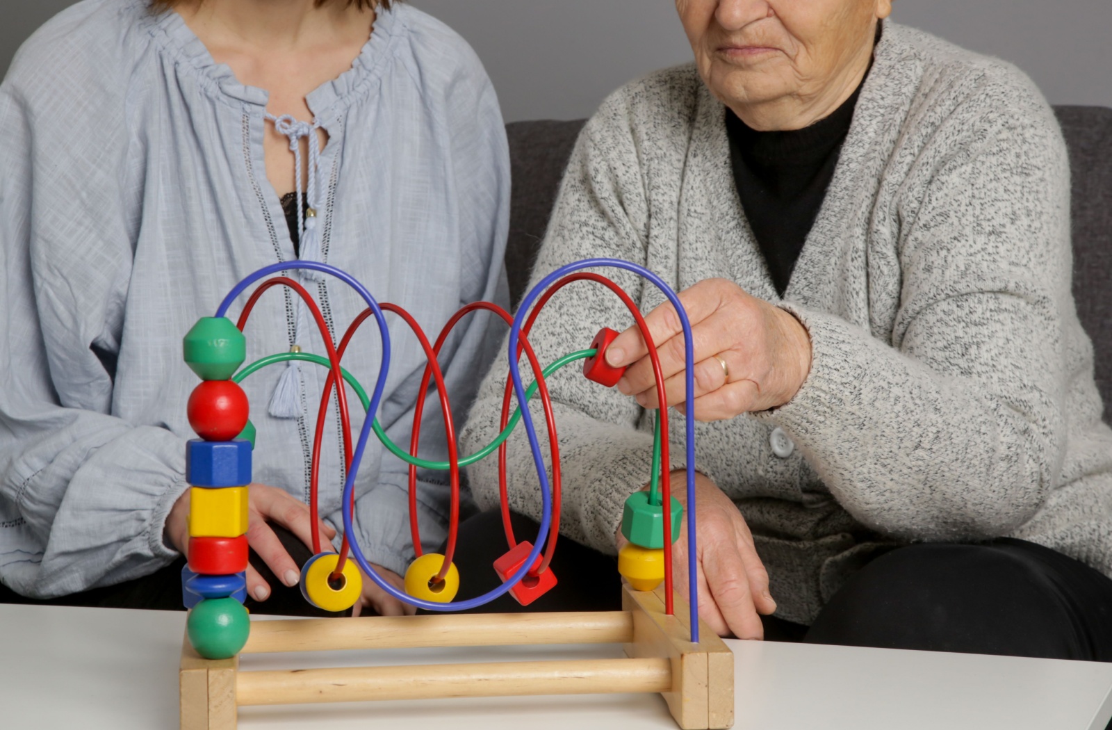 A friend supports a senior with dementia while they play with a child’s toy as a means of supporting memory function