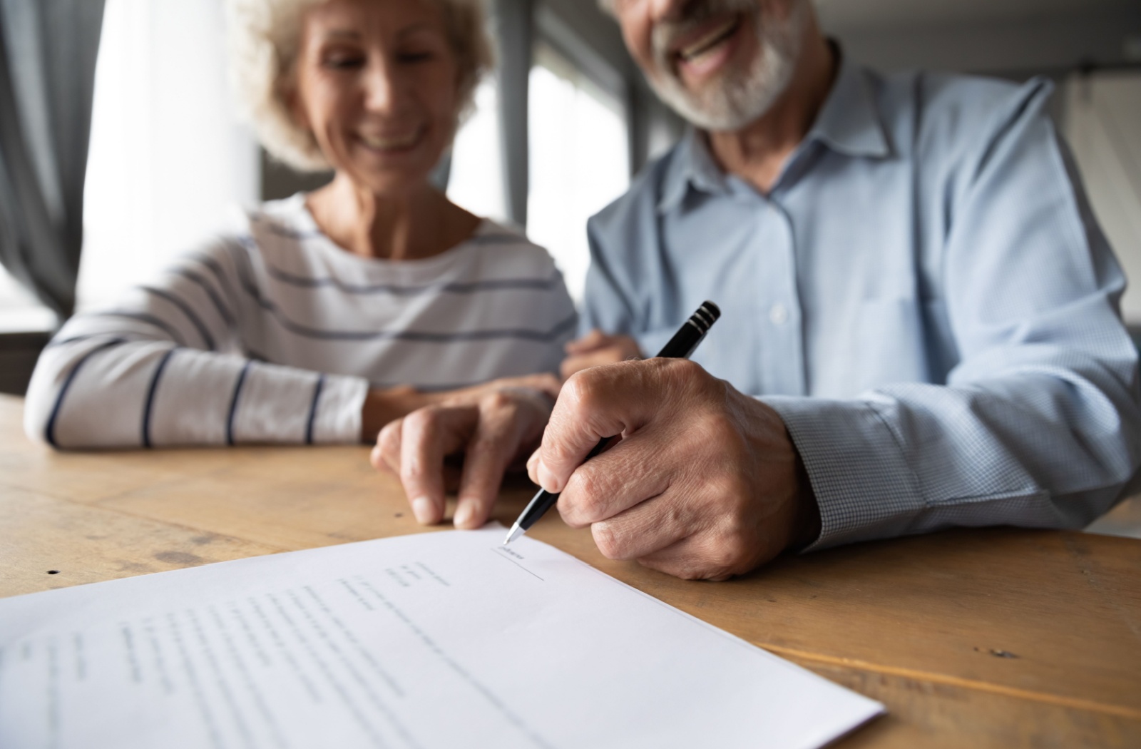 Close-up view of a smiling senior couple preparing to sign legal documents after a dementia diagnosis